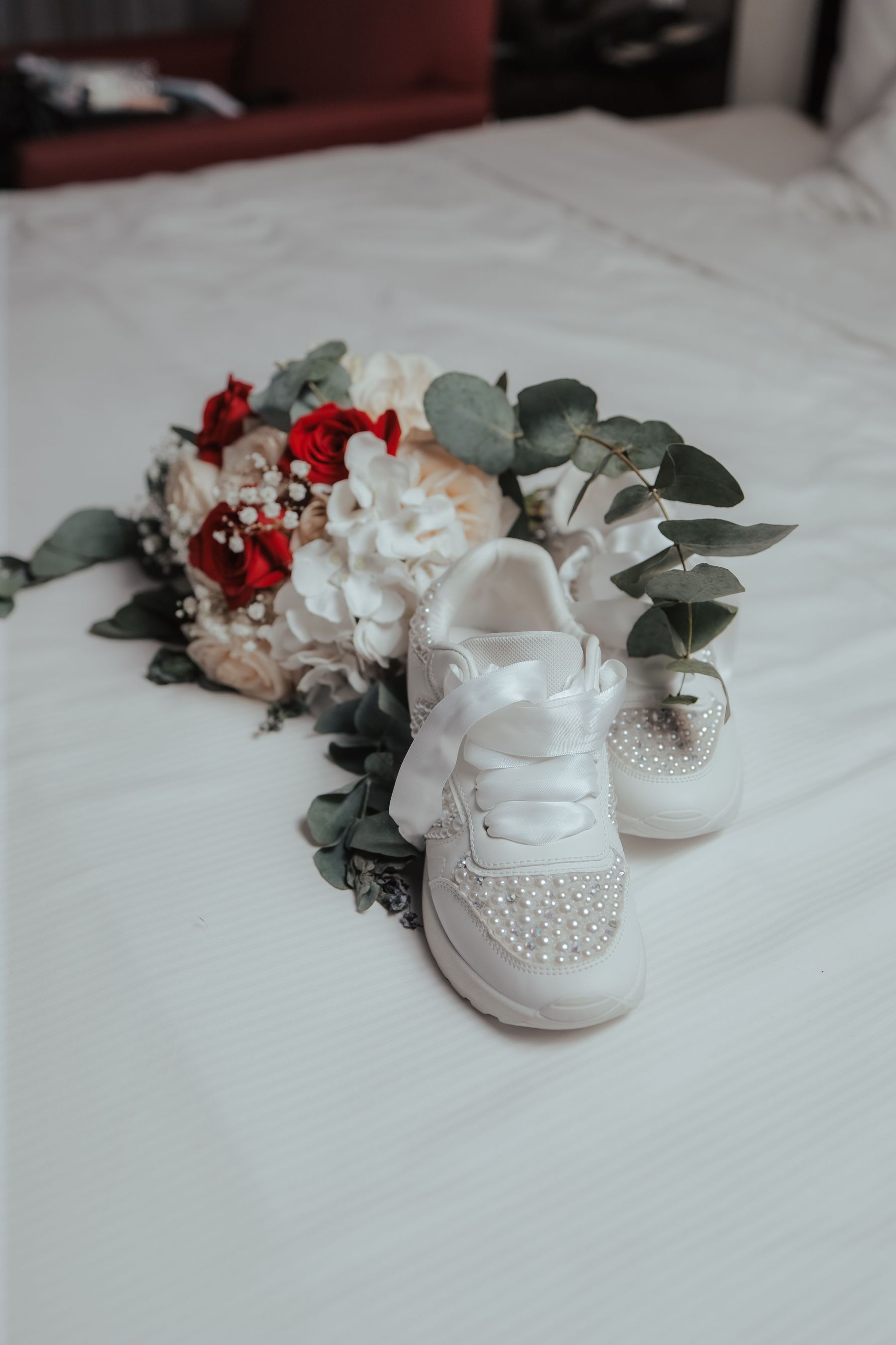 Braut-Sneaker mit Perlen und Strass neben Brautstrauß mit roten Rosen